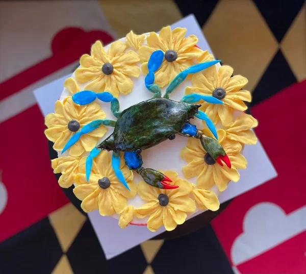 A custom cake decorated with yellow piped flowers and a detailed blue and green crab figurine.