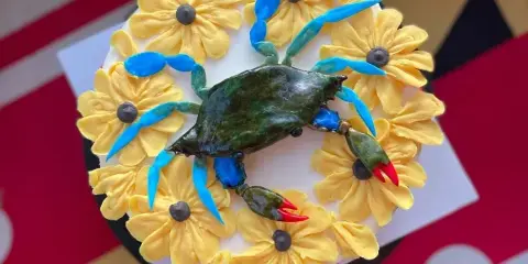 A custom cake decorated with yellow piped flowers and a detailed blue and green crab figurine.
