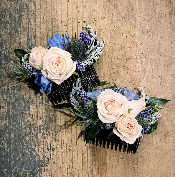 Two floral hair combs with cream roses and blue flowers on a rustic wooden background