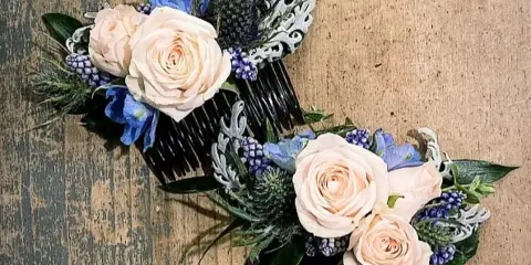 Two floral hair combs with cream roses and blue flowers on a rustic wooden background
