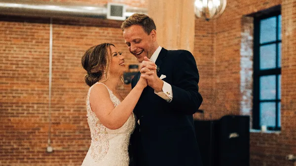 A bride and groom dancing in a rustic ballroom with exposed brick walls.