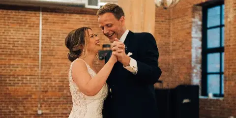 A bride and groom dancing in a rustic ballroom with exposed brick walls.