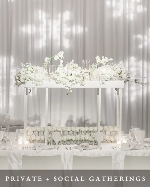 Elegant white event table with floral centerpiece and glassware in a draped venue setting