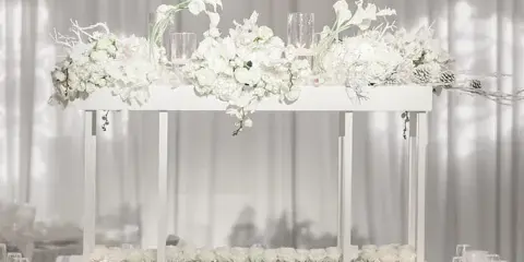 Elegant white event table with floral centerpiece and glassware in a draped venue setting