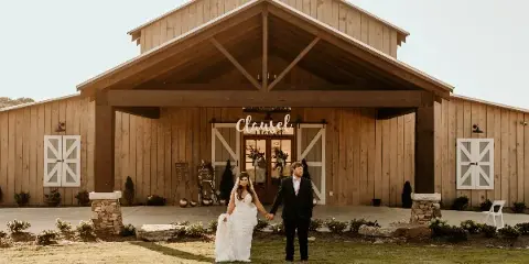 A bride and groom standing in front of a large wooden barn wedding venue with a 'Classel' sign above the entrance.