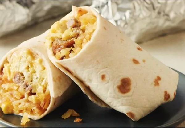 Two breakfast burritos cut in half to reveal a filling of scrambled eggs, potatoes, and sausage, served on a dark plate.