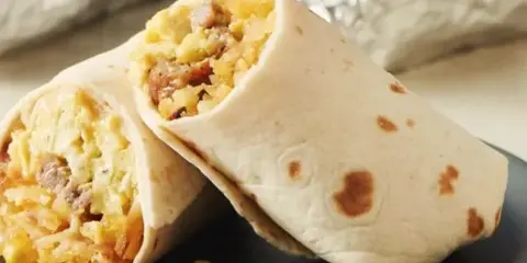 Two breakfast burritos cut in half to reveal a filling of scrambled eggs, potatoes, and sausage, served on a dark plate.