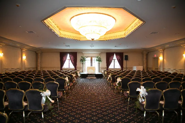 Interior of a large banquet hall with rows of chairs arranged for a wedding ceremony, featuring a chandelier and decorative floral arrangements.