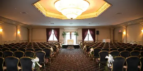 Interior of a large banquet hall with rows of chairs arranged for a wedding ceremony, featuring a chandelier and decorative floral arrangements.