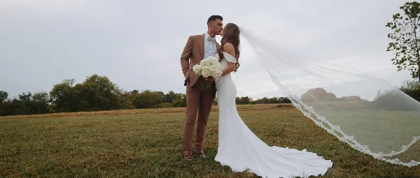 A bride and groom sharing a kiss in a grassy field, with the bride holding a bouquet of white roses.