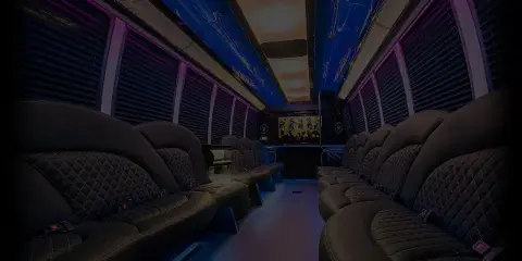 Interior view of a party bus with rows of black leather seats and purple ambient lighting.