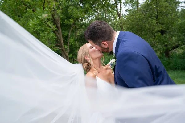 A bride and groom sharing a kiss outdoors with the bride's veil flowing in the foreground.