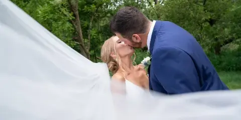 A bride and groom sharing a kiss outdoors with the bride's veil flowing in the foreground.