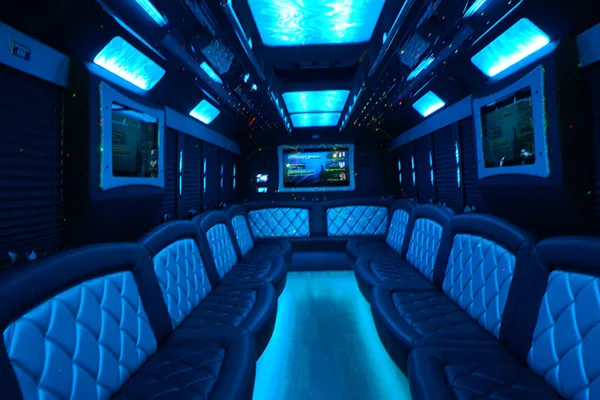 Interior view of a party bus featuring blue ambient lighting and leather bench seating.
