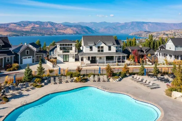 Aerial view of a resort swimming pool and surrounding vacation homes overlooking a lake and mountains.