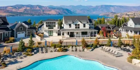 Aerial view of a resort swimming pool and surrounding vacation homes overlooking a lake and mountains.