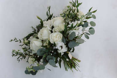 A wedding bouquet composed of white roses, white filler flowers, and green eucalyptus stems.