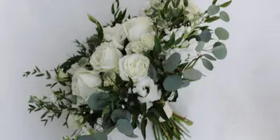 A wedding bouquet composed of white roses, white filler flowers, and green eucalyptus stems.