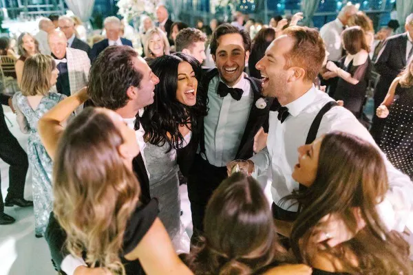 A group of wedding guests dancing and laughing on a dance floor at a reception.