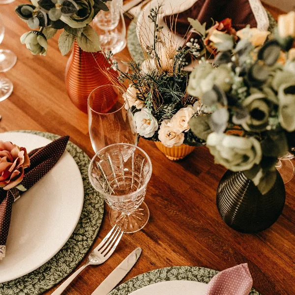 A close-up view of an elegant event table setting featuring floral arrangements, glassware, and patterned placemats on a wooden table.