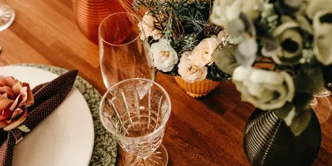 A close-up view of an elegant event table setting featuring floral arrangements, glassware, and patterned placemats on a wooden table.