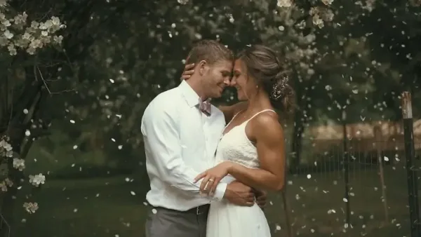 A cinematic photograph of a bride and groom embracing outdoors with falling petals.