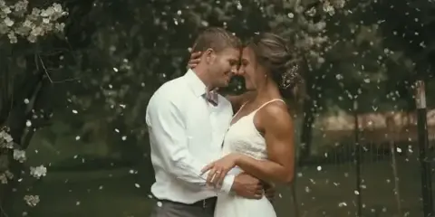 A cinematic photograph of a bride and groom embracing outdoors with falling petals.