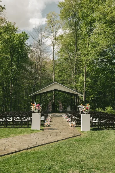 Outdoor wedding ceremony setup with a gazebo, rows of chairs, and floral arrangements in a wooded clearing