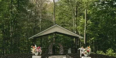Outdoor wedding ceremony setup with a gazebo, rows of chairs, and floral arrangements in a wooded clearing