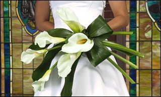 A bride in a white dress holding a bouquet of white calla lilies.