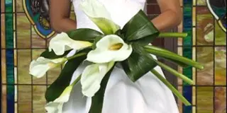 A bride in a white dress holding a bouquet of white calla lilies.