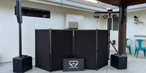 Outdoor DJ setup with black booth panels, tall speakers, lighting truss, and a Crown Entertainment branded flight case.