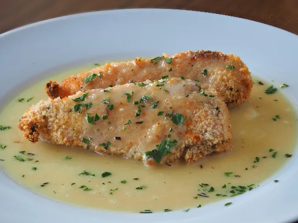A plate of panko crusted chicken served with a light sauce and garnished with fresh herbs.