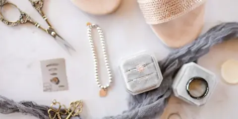 A flat lay photograph of wedding accessories including a diamond ring, wedding bands, pearl necklace, and bridal heels.