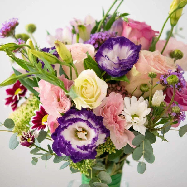 A close-up of a floral bouquet containing pink and white roses, purple and white lisianthus, and eucalyptus greenery.