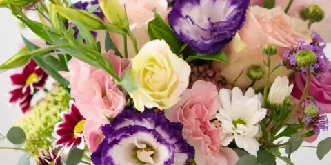 A close-up of a floral bouquet containing pink and white roses, purple and white lisianthus, and eucalyptus greenery.