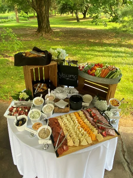 An outdoor catering table set with a large charcuterie board, vegetable tray, and assorted dips.