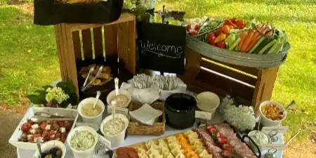 An outdoor catering table set with a large charcuterie board, vegetable tray, and assorted dips.