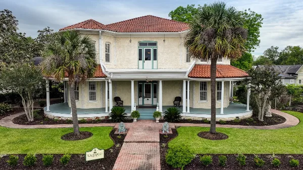 Exterior view of The Caldwell House, a historic two-story estate with a red-tiled roof, white columns, and a brick walkway leading to the front porch.