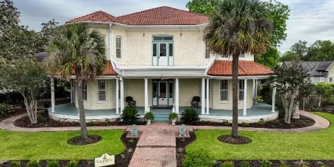 Exterior view of The Caldwell House, a historic two-story estate with a red-tiled roof, white columns, and a brick walkway leading to the front porch.