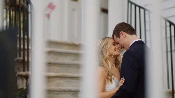 A bride and groom sharing a tender moment on stone steps, framed by white columns.