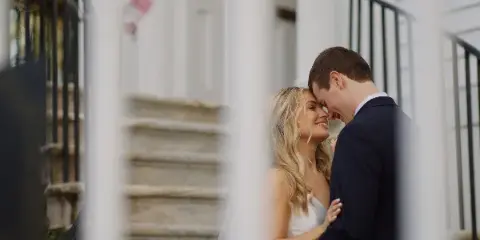 A bride and groom sharing a tender moment on stone steps, framed by white columns.