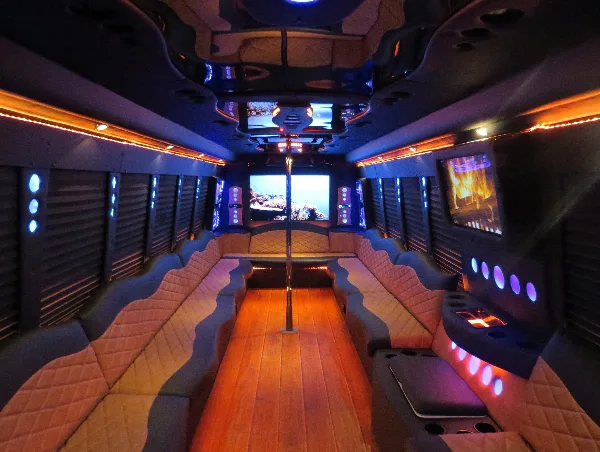 Interior view of a party bus with quilted bench seating, wood flooring, and colorful LED lighting.