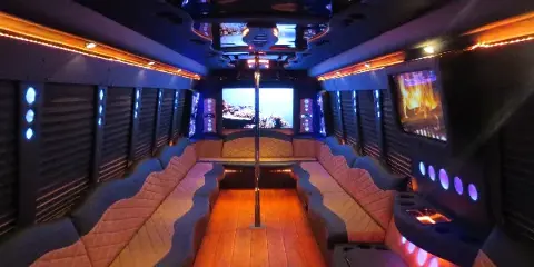 Interior view of a party bus with quilted bench seating, wood flooring, and colorful LED lighting.