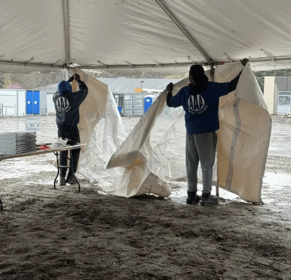 Two workers in branded shirts setting up a white event tent and handling linens outdoors.