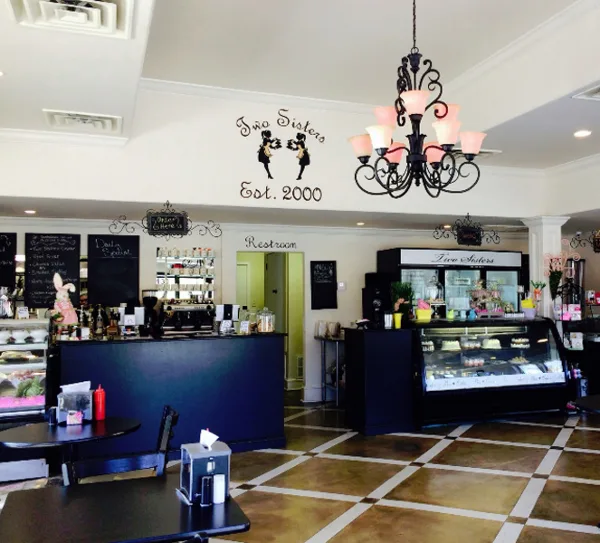 Interior view of the Two Sisters Cafe showing the service counter, pastry display case, and branded wall sign.