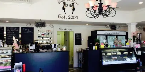 Interior view of the Two Sisters Cafe showing the service counter, pastry display case, and branded wall sign.