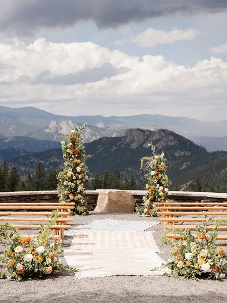 Outdoor wedding ceremony setup with floral arrangements and wooden benches overlooking a mountain range.
