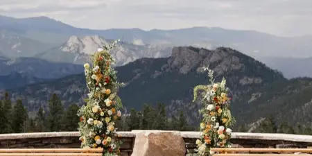 Outdoor wedding ceremony setup with floral arrangements and wooden benches overlooking a mountain range.