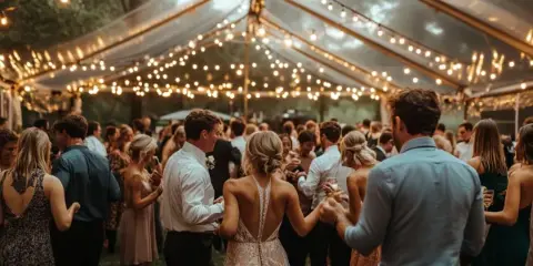 Guests dancing at a wedding reception under a tent with string lights.
